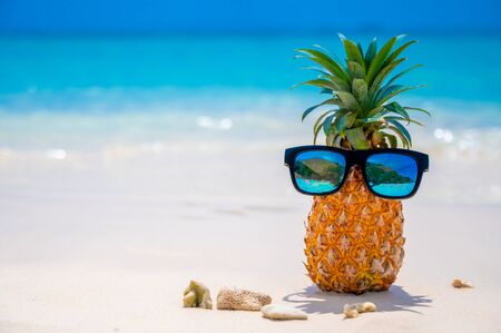 Glasses pineapples are located on the beach by the sea in the hot sun, setting the concept for summer.の写真素材