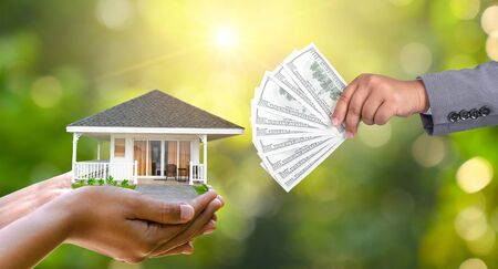 The hands of a businessman hold money and the other hand holds a house. The idea of saving money to buy a houseの写真素材