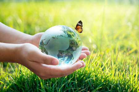 A man with a glass globe Concept day earth Save the world save environment The world is in the grass of the green bokeh backgroundの写真素材