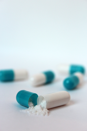 Tablet of blue color uncovered and powder in the foreground medicine treatmentの写真素材