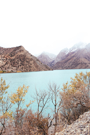 Lake on the background of mountains with cloudy sky and autumn treesの写真素材