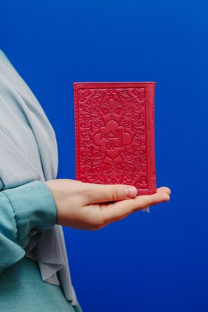 Muslim woman in a headscarf holds a Quran in her hands on a pink backgroundの写真素材