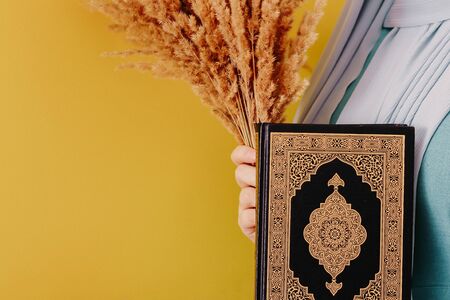 Muslim woman in a headscarf holds a Quran in her hands on a pink backgroundの写真素材