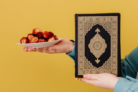 Muslim girl in a scarf holds dates and Quranの写真素材