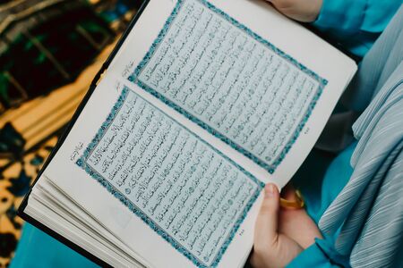 Muslim woman in a headscarf holds a Quran in her hands on a pink background