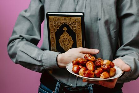 The guy holds the Holy Quran, Islamic rosary and dates. On a pink background.の写真素材