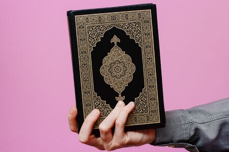The guy holds the Holy Quran. On a pink background.