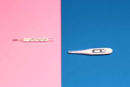 two thermometers, one mercury and the other electronic on a pink and blue backgroundの写真素材