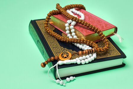 Two Quranes of blue and pink color with muslim rosary on a green background