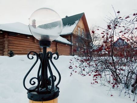 Round street lamp on the background of an old wooden house. Near a tree with mountain ashの写真素材