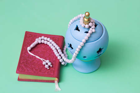 Blue candlestick and muslim rosary and quran on green background