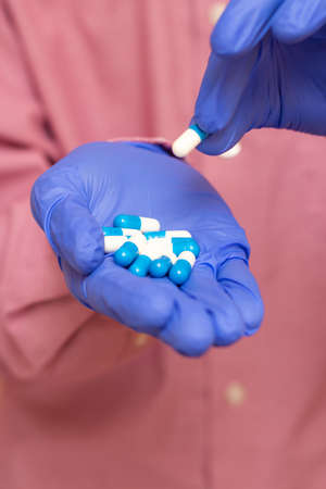 A guy in a medical mask and gloves holds white-blue tablets. Medical content. Pink background