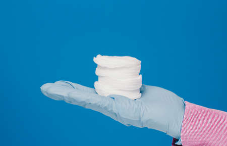 A guy in a medical glove holds cotton pads. Blue background. Medical and cosmetology contentの写真素材