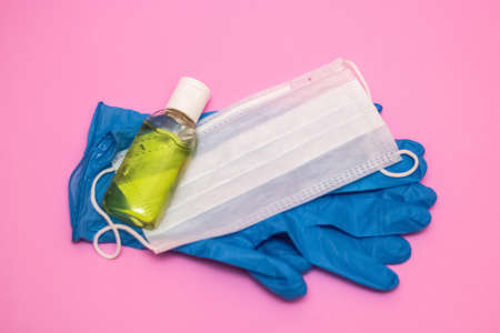 Hand antiseptic and white face mask on a pink background