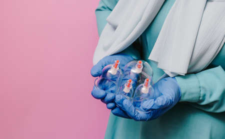 A girl in a scarf holds in her hands jars for hijama. Vacuum pumps dropping