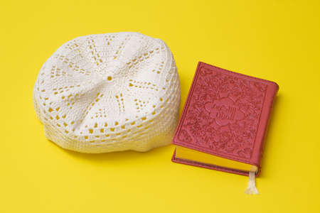 Pink quran and white skullcap on a yellow backgroundの写真素材