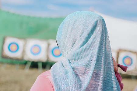 A girl in a hijab against the background of targets for archery and arbalest. Muslim woman in a blue...