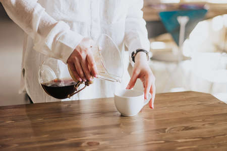 A girl in a white shirt pours coffee into the porridge. Chemex. Alternative ways of brewing coffee. Coffee shop conceptの写真素材