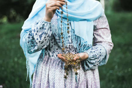 A Muslim woman in a blue dress holds a garland with stars in her hands. Against the background of the forest.の写真素材
