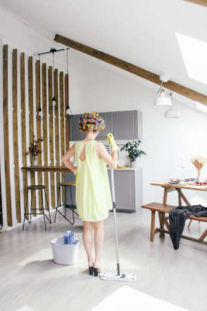 The girl in hair curlers washes floors in the kitchen mop