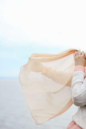 The girl waves a scarf in the wind against the background of the sea and sky.