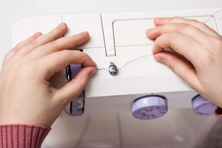 The girl is threading the needle of a sewing machine. Close plan. White sewing machine. Sewing content.の写真素材