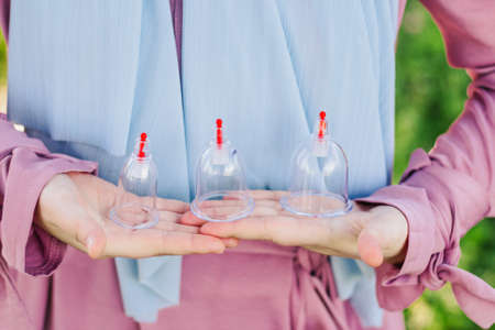 The girl is holding a jar for hijama. Hijama, bloodletting, treatment of sunna. Jars for bloodletting against the background of trees and greenery.の写真素材