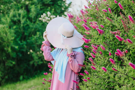 Muslim girl with a hat on a background of pink flowers. Islam. Muslim woman in a pink dress and a...
