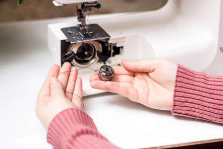 The girl is threading the needle of a sewing machine. Close plan. White sewing machine. Sewing...