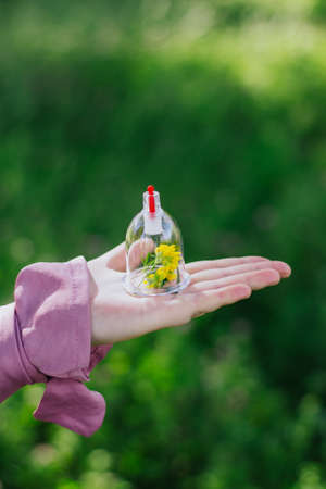 The girl holds a jar for a hijama and a flower in her hands. Yellow flowers. Hijama, bloodletting, treatment of sunna. Jars for bloodletting against the background of trees and greenery.の写真素材