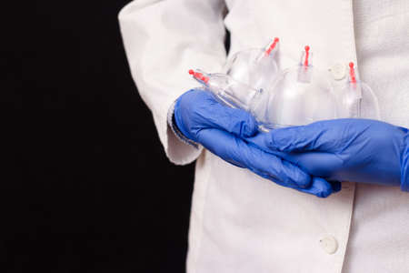 Jars for hijama, bloodletting in the hands of a doctor in a white coat on a black background. Hijama according to the Sunnah. Hajjamの写真素材