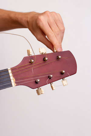 The guy is tuning the guitar. Close plan. Wooden guitar.