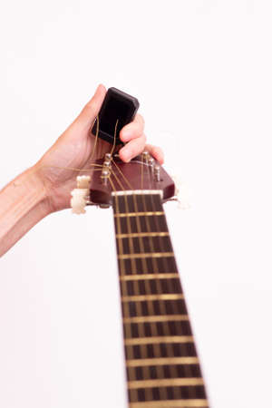 Guitar tuner. Wooden guitar on a white background. Guitar tuning. The guy tunes the guitar.の写真素材
