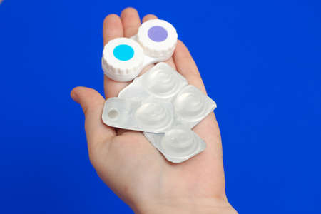 A container for contact lenses and lenses on the hands of a woman on a blue background