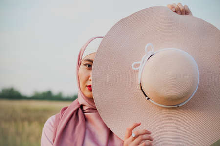 Muslim woman in a pink hijab on the field with a straw hat. Close plan