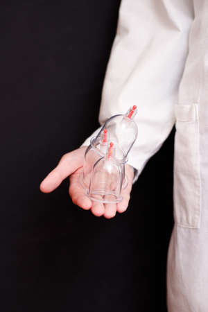 Jars for hijama bloodletting in the hands of a doctor in a white coat on a black background. Hijama according to the Sunnah. Hajjamの写真素材
