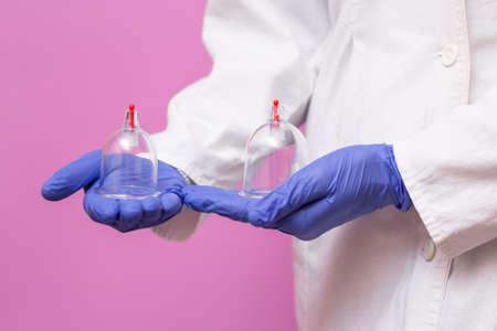 Jars for hijama bloodletting in the hands of a doctor in a white medical coat on a pink background. Hijama according to the Sunnah. Hajjamの写真素材