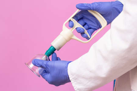 Jars for hijama bloodletting and pumps on the hands of a doctor in a white medical coat on a pink background. Hijama according to the Sunnah. Hajjamの写真素材