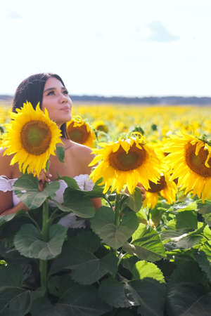 Beautiful brunette woman in a white top on the field with sunflowers. Yellow sunflowers. Close plan.の写真素材