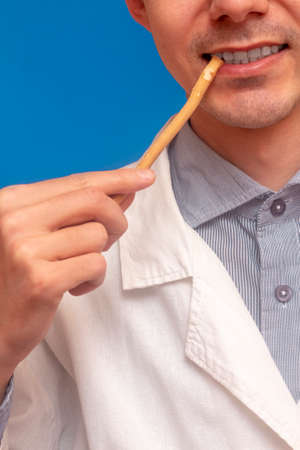 A young man brushes his teeth with a miswak siwak in a white coat. arak tree, Salvadora persica, sunnah. Blue backgroundの写真素材