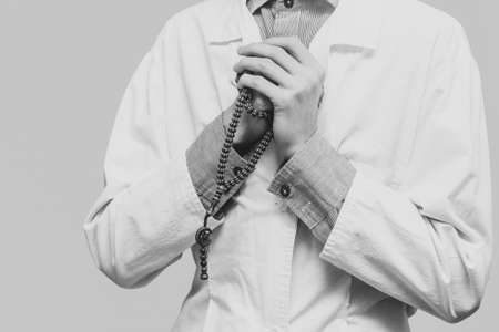 A young man in a white robe raised his hands up and prayed with a Muslim rosary. Medical gloves. Doctor praying. A Muslim makes dua. Black and white photo.の写真素材