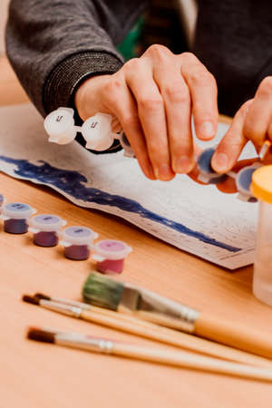 The guy paints a picture by numbers. Watercolor paints. Painting brush, Painting by numbers conceptの写真素材