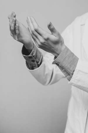 A young man in a white medical coat raised his hands and prayed. Medical gloves. The doctor is praying. A Muslim makes dua. Black and white photoの写真素材