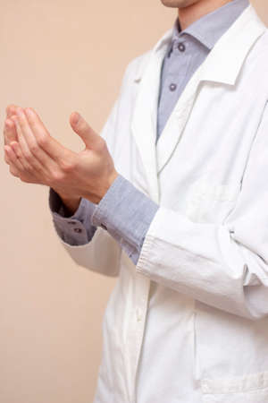 A young man in a white coat raised his hands up and pray. Beige background. Doctor praying. A Muslim makes dua.の写真素材