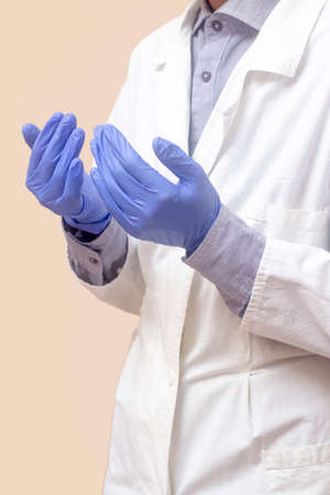 A young man in a white medical coat raised his hands and prayed. Medical gloves. Beige background. The doctor is praying. A Muslim makes duaの写真素材
