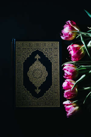 Holy Quran on a black background. Pink tulips. Hard light. The month of Ramadan. Islamic concept. The religion is Islam. Book of Muslimsの写真素材