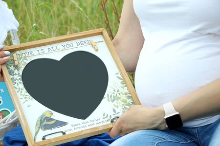 Pregnant woman in white t-shirt holding a blank heart - shaped boardの写真素材