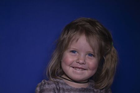 portrait of happy a three year old blond girl with blue eyes on a blue background