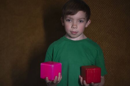 portrait of a nine year old blond boy in a green t-shirt on brown background holding a few multicoloured cubesの写真素材