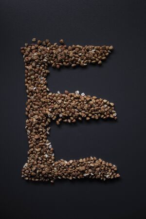 Letter E written with buckwheat On gray background, top view, copy space. Food supplies crisis, food donation on quarantine isolation periodの写真素材